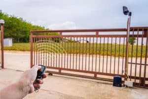 Hand using a remote control to open an automated sliding metal entrance gates.