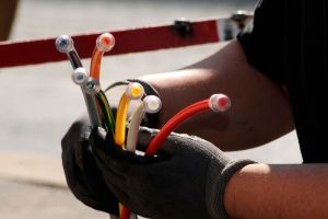 Technician wearing gloves holds multiple color-coded fiber optic cables, highlighting measures for fiber optic cable protection. The image emphasizes the handling and safeguarding of fiber optic cables during harsh conditions.