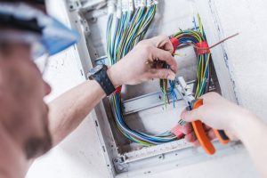 Electrician working on a wiring panel with various coloured cables, demonstrating the best outdoor cable installation practices in the UAE.