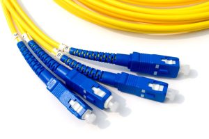 Close-up of yellow fiber optic cables with blue connectors, demonstrating the importance of fiber optic cable protection for reliable data transmission. The image showcases the durability and design of fiber optic cables essential for protection against harsh environmental conditions.