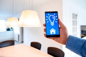 A person using a smartphone to control smart home lighting, shown with illuminated modern pendant lights in a bright room.