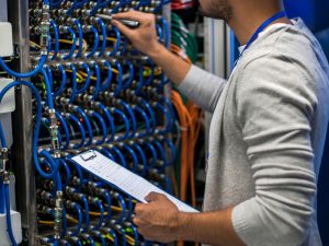 Technician inspecting IT networking cables and infrastructure in a data center for maintenance.