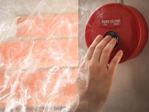 A hand pressing a red fire alarm button highlights the importance of installing a fire alarm system.